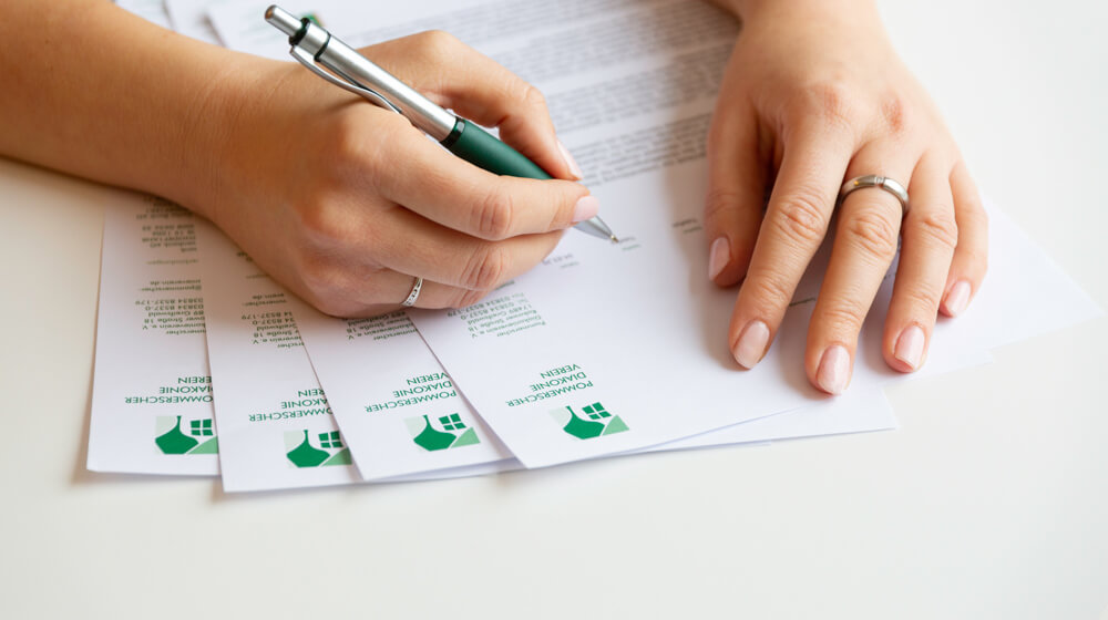 Zwei Hände liegen auf Briefbögen. Eine Hand hält einen Stift