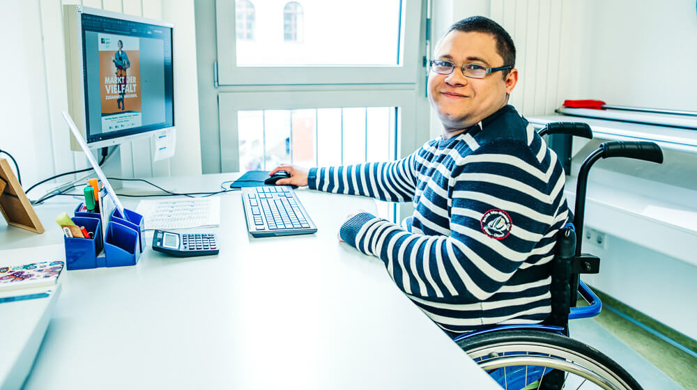 Ein Mitarbeiter in unserem Copyshop in Greifswald arbeitet in seinem Rollstuhl am PC