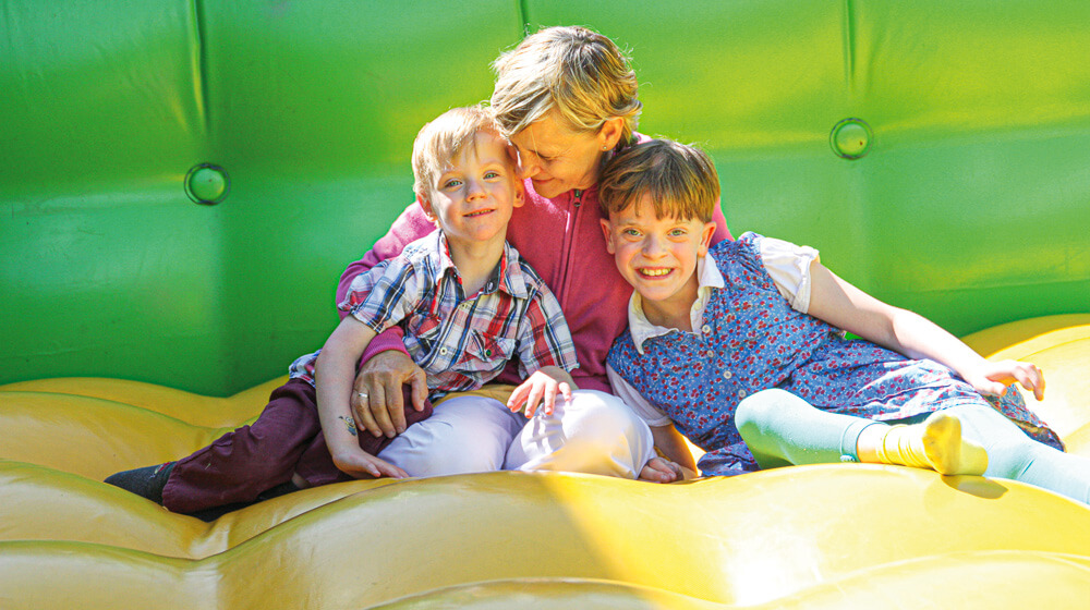 Frau mit zwei lächelnden Kindern sitzt in einer Hüpfburg bei einer Veranstaltung des Pommerschen Diakonievereins