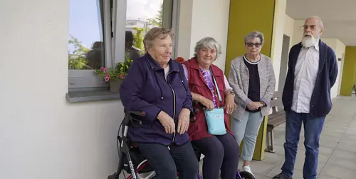Eine Gruppe von vier Senioren auf einem Hausflur, zwei sitzen auf einem Rollator, zwei stehen