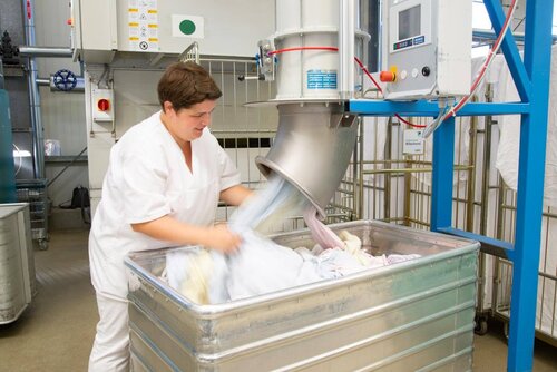 Aus einer Röhre fliegt frische Wäsche und wird von einer Mitarbeiterin in einen großen Behälter gelegt