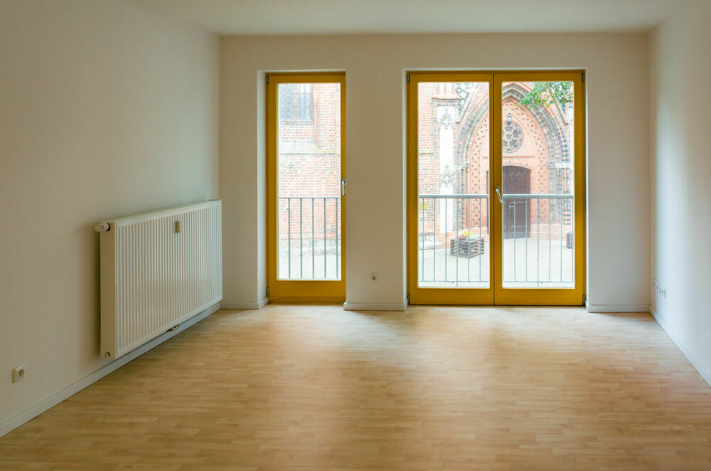 Ein leeres Wohnzimmer mit Fußboden, Heizkörper und Fenster