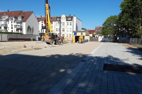 Ein großer Kran steht auf dem sandigen Bauplatz. Im Vordergrund Pflasterung des Grundstücks