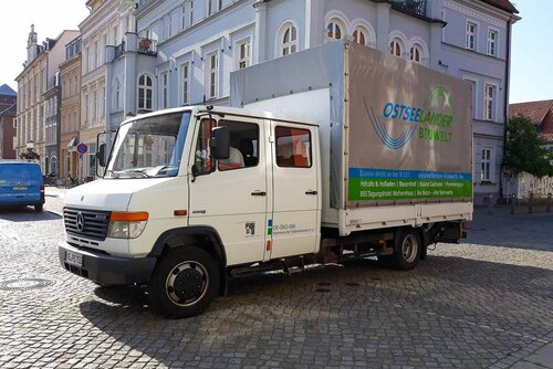 Ein großer LKW mit Plane steht vor Gebäuden auf dem Greifswalder Marktplatz