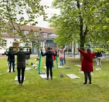 Eine Gruppe steht in einem Garten und macht Sportübungen mit einer Matte