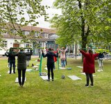 Eine Gruppe steht in einem Garten und macht Sportübungen mit einer Matte