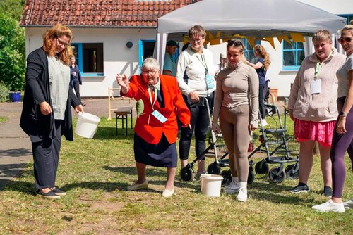 Eine ältere Dame wirft einen Ball, während andere Senioren sie dabei beobachten und sie andere Personen unterstützen