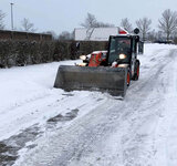 Ein Radlader mit einer großen Schaufel fährt über einen frisch vom Schnee geräumten Weg