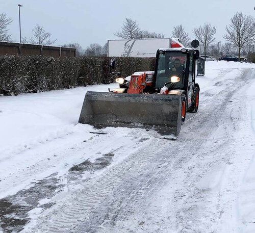 Ein Radlader mit einer großen Schaufel fährt über einen frisch vom Schnee geräumten Weg