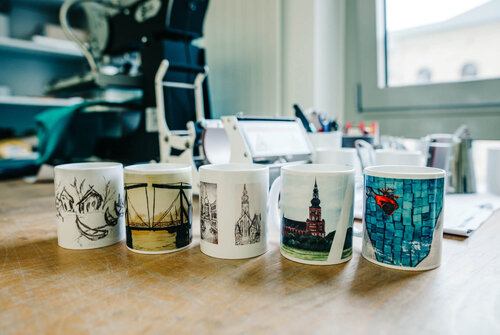 Fünf Tassen stehen mit farbigen Motiven bedruckt nebeneinander