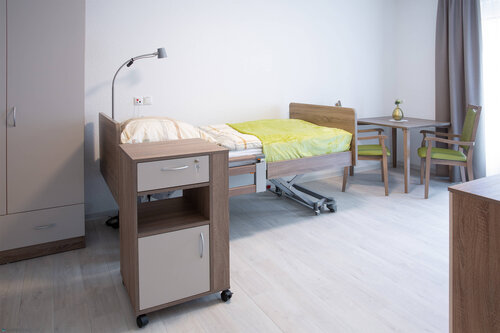 Ein Zimmer mit Bett, Tisch und Rollcontainer