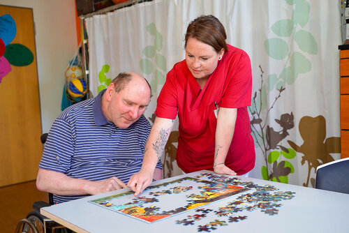 Eine Pflegefachfrau hilft einem Mann beim Puzzeln an einem Tisch