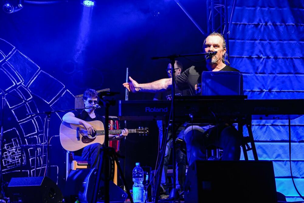 Micha Turban sitzt bei einem Konzert am Keyboard und streckt den Arm nach hinten, um die Band vorzustellen