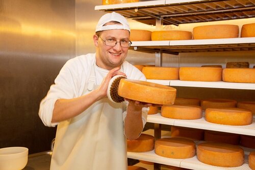 Ein Mann mit Schürze hält einen Käselaib und reibt ihn mit Salz ein