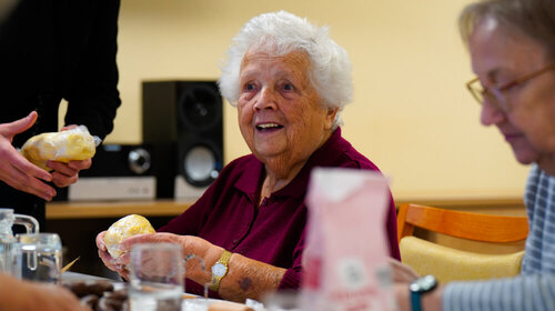 Eine ältere Dame sitzt an einem Tisch und knetet ein Stück Teig