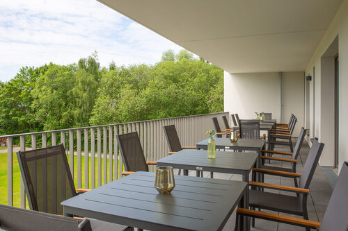 Ein überdachter Balkon mit mehreren Gartentischen und Stühlen