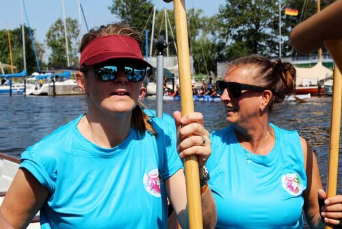 Zwei Frauen mit Cape und Sonnenbrille halten jeweils ein Paddel