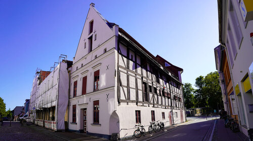 Ein altes Fachwerkgebäude mit drei Stockwerken und einem Giebeldach inmitten einer Stadt