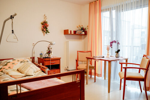 Einzelzimmer mit Pflegebett, Sitzecke und Aufstehhilfe