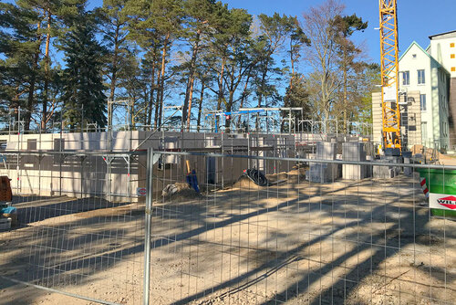 Der Rohbau des Erdgeschosses aus großen Steinen hinter einem Bauzaun