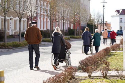 Eine kleine Gruppe von Menschen, teils mit Rollstuhl, teils zu Fuß, gehen auf einem Fußweg in Jarmen