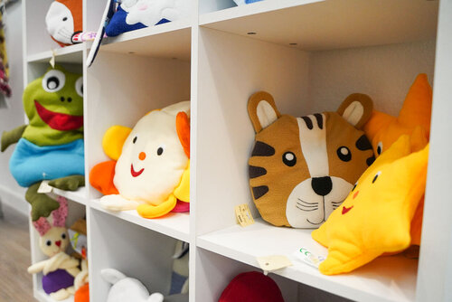 In einem Regal liegen Kuschelkissen in verschiedenen Tierformen