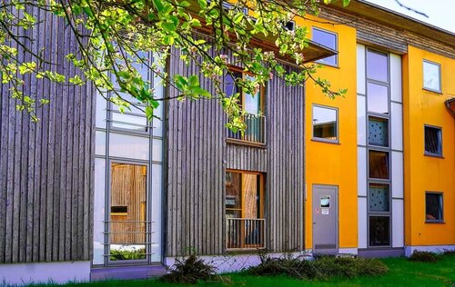 Ein Haus mit drei Stockwerken und einer Holzverkleidung, davor eine Rasenfläche