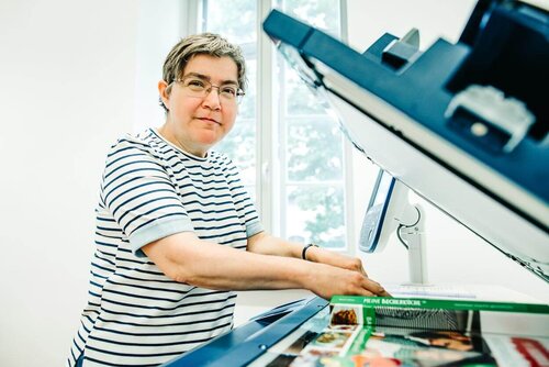 Eine Mitarbeiterin legt eine Zeitung zum Kopieren auf den Kopierer