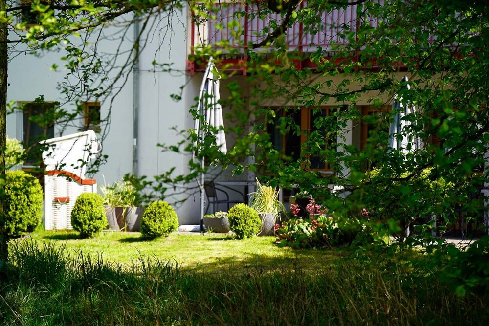 Ein Baum, Strandkorb und Büsche vor einem Gebäude der Züssower Wohnstätten