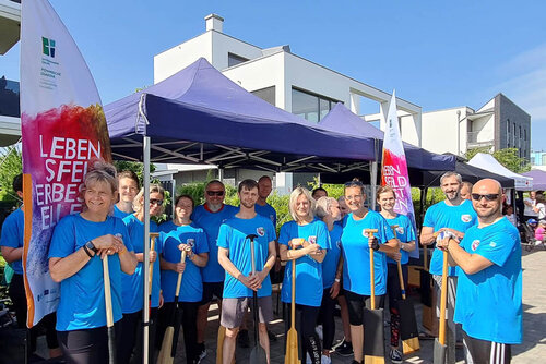 Menschen in Sportkleidung stützen sich auf ihre Paddel und stehen vor einem Zelt