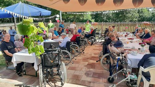 Viele Menschen sitzen an gedeckten Tischen unter einem Pavillon.