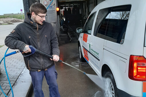 Ein junger Mann spritzt mit einem Hochdruckreiniger ein Auto ab