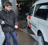 Ein junger Mann spritzt mit einem Hochdruckreiniger ein Auto ab