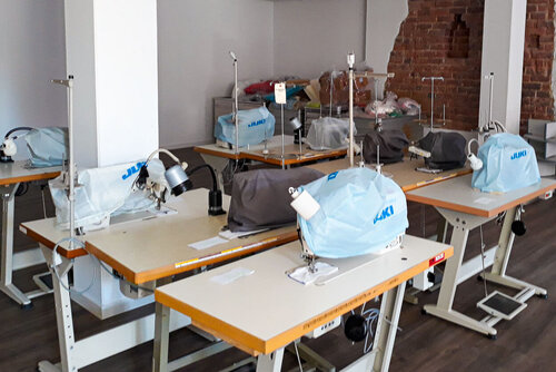 Mehrere Tische stehen nebeneinander und darauf mit einer Schutzhülle verpackte Nähmaschinen