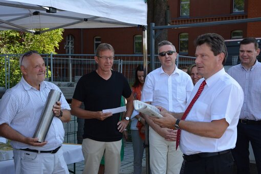 Vier Menschen stehen beieinander und einer hält eine große Hülse und ein anderer eine Zeitung.