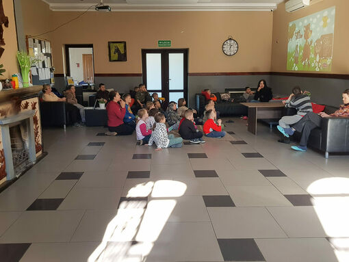Eine Gruppe von Kindern sitzt auf einem großen Fliesenboden und schaut an der Wand auf einen projizierten Kinderfilm