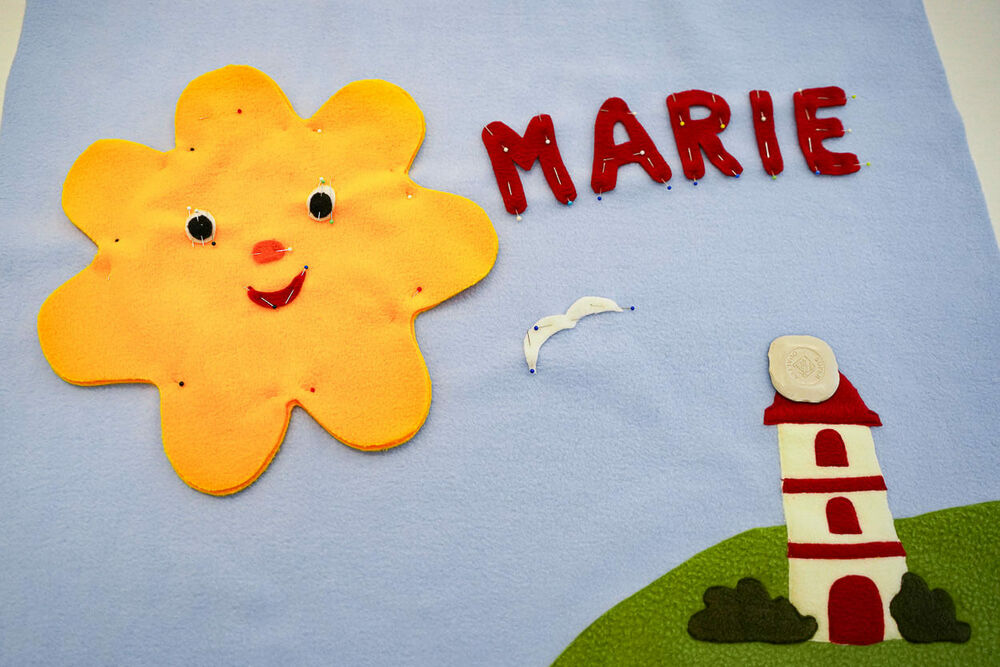 Aus Stoff ist auf einer Decke eine Sonne, ein Leuchtturm und der Name "Marie" abgebildet