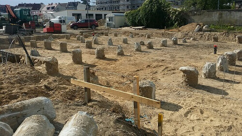 Auf einer sandigen Fläche stehen viele große Betonstützen