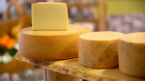 Verschiedene Käsesorten liegen auf einem Regalbrett. Ein großes Stück Käse liegt aufgeschnitten auf ihnen.