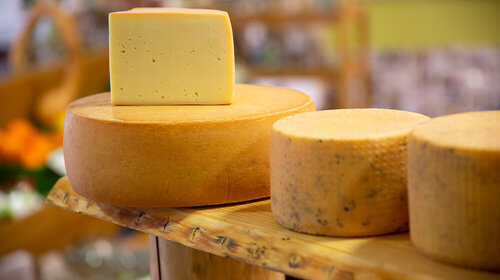 Frische Käselaibe der Sorte Strandtaler Verschiedene Käsesorten liegen auf einem Regalbrett. Ein großes Stück Käse liegt aufgeschnitten auf ihnen.