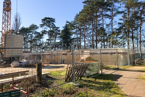 Der Rohbau des Erdgeschosses aus großen Steinen hinter einem Bauzaun