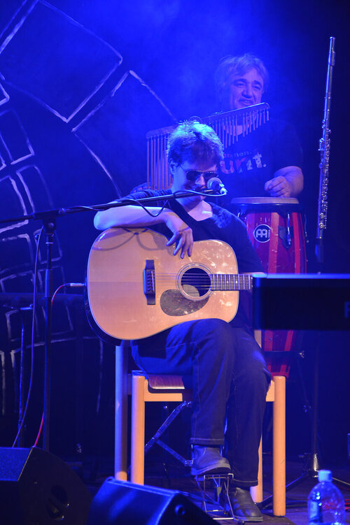 Nicole Vollbrecht sitzt bei einem Konzert auf einem Stuhl und spielt akustische Gitarre.
