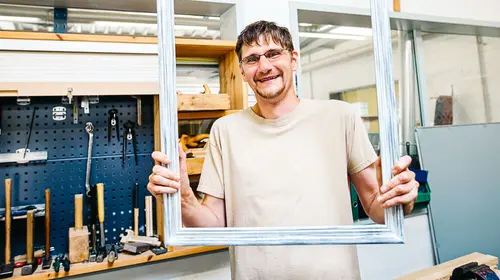 Ein Mann hält einen Holzrahmen in die Höhe und schaut durch ihn hindurch