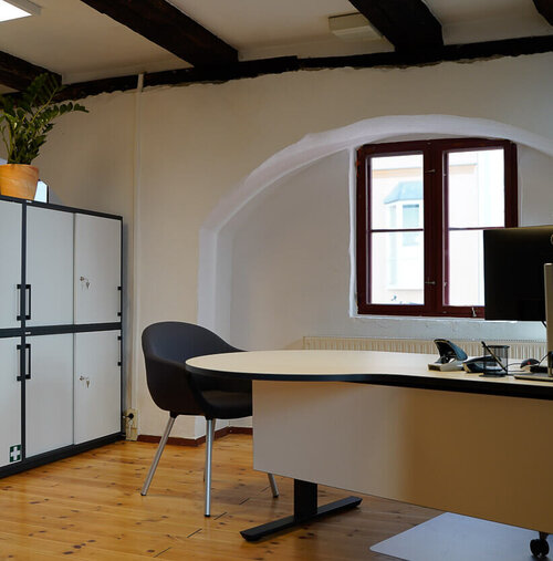 Ein Arbeitstisch mit einem PC, einem Sessel und Schränken