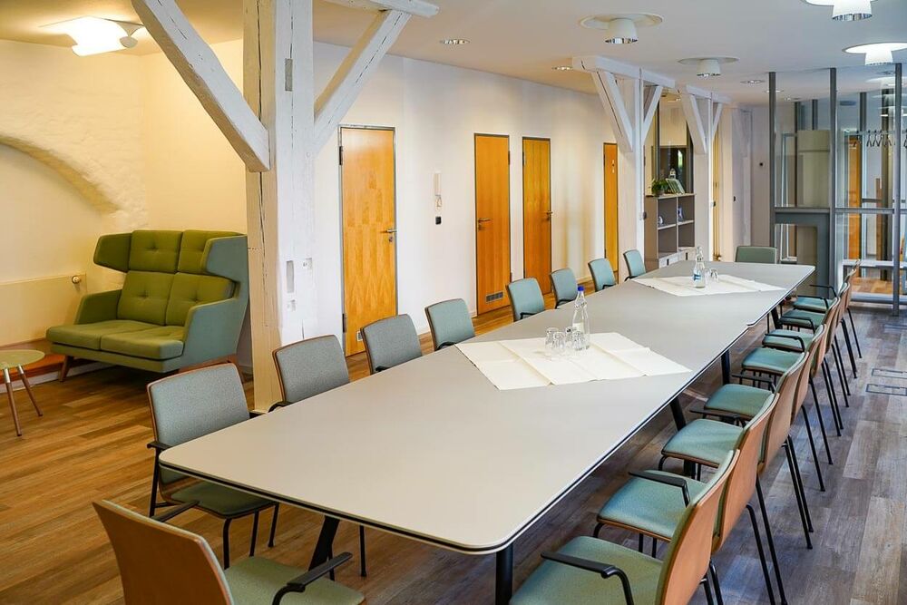Ein langer Konferenztisch im Tagungsraum Netzwerk mit Stühlen und einer Sitzecke links