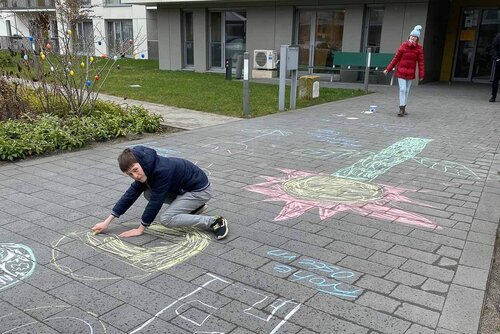 Ein Junge malt mit Kreise eine Form auf ein Pflaster und ein Mädchen hilft ihm