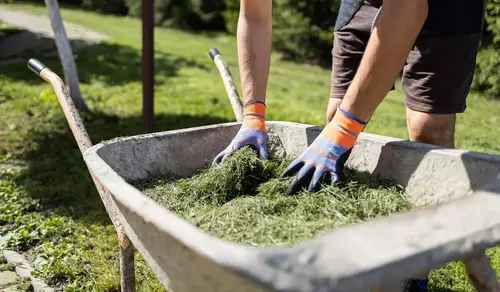 Ein Mann mit Handschuhen und Arbeitskleidung kniet auf dem Boden und rollt eine Rolle Rollrasen aus