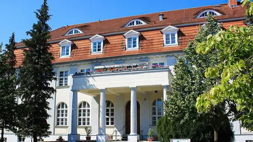 Eine alte Villa mit Säulen, links und rechts Bäume 