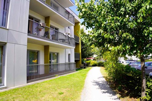 Ein Fußweg läuft entlang eines Rasens und eines Baumes am Gebäude des Pflegeheims vorbei