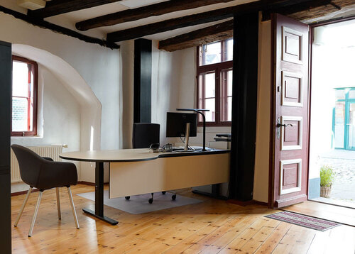 Ein großer Schreibtisch mit Sesseln, einem alten Holzfußboden und einer göffneten Tür